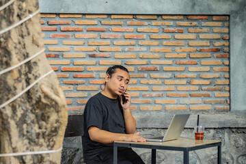 Young asian men, digital nomad working remotely from a cafe, drinking coffee and using laptop.