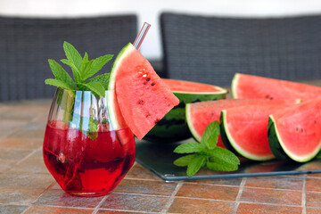 Iced red cocktail or cold watermelon drink with mint leaves, refreshing summer drink served with sliced watermelon