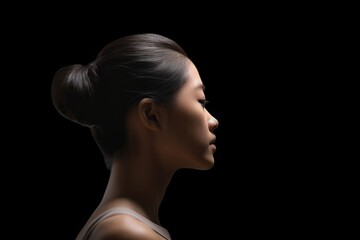 a japanese young woman looks up on isolated black background. a profile of ballerina, her hair pulled into a bun. the concept of hope, mental health, copy space