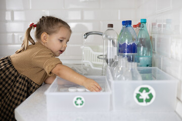 A small child sorts plastic into boxes with a recycling sign. In the kitchen, a child takes part in sorting plastic for recycling. An enthusiastic child helps sort plastic for recycling.