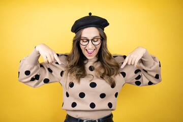 Young beautiful brunette woman wearing french beret and glasses over yellow background surprised,...