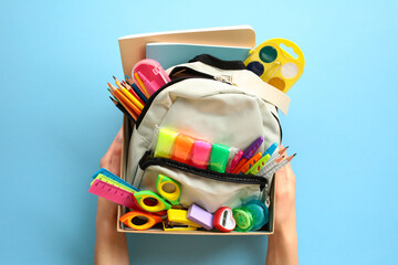School supplies donation concept. Backpack with school supplies in cardboard box in women's hands...