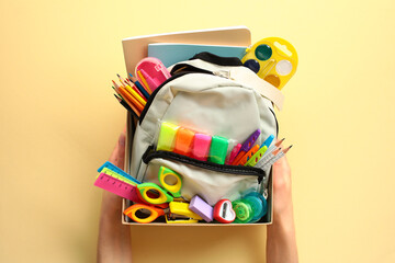 The woman's hands hold a donation box with a backpack containing various school supplies. Donation concept.