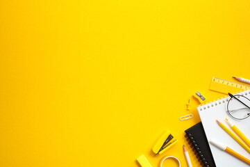 Vibrant workspace with office supplies on yellow background. Flat lay paper notebooks, eyeglasses,...