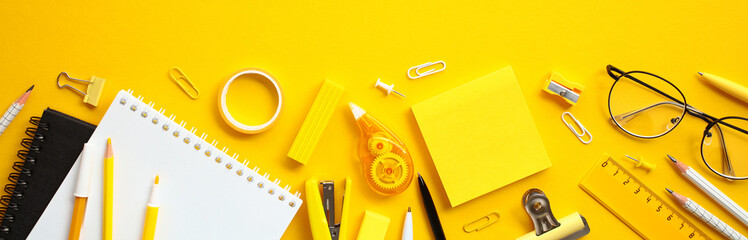 Flat lay office supplies on yellow background. Wide banner with paper notebook, ruler, pens,...