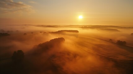 Aerial view of a sunrise casting golden light over foggy fields and trees
