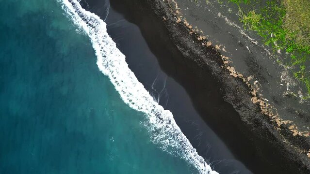 Drone Shot Diagonal of Black Sand Beach and some gras behind in Indonesia. Aerial View Top Down waves crushing. . High quality 4k footage