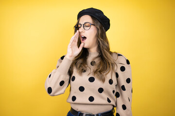 Young beautiful brunette woman wearing french beret and glasses over yellow background bored...