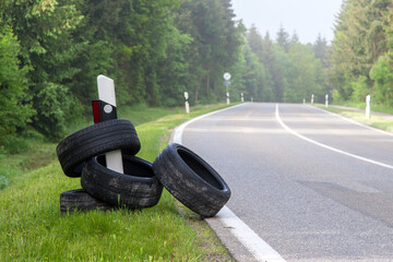 Along a country road, several illegally dumped old tires are stuck on a roadside marker. This...