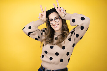 Young beautiful brunette woman wearing french beret and glasses over yellow background Posing funny...