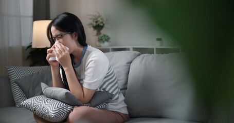 Portrait of Unwell young woman having a cold, sneezing and blowing your nose while sitting on sofa...
