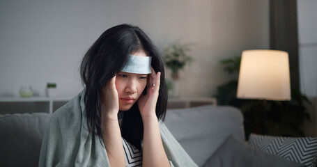 Portrait of Unwell young woman have a high fever and massaging temples to relieve headache ,wrapped...