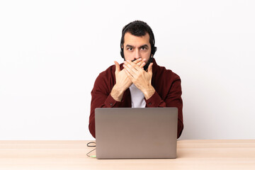 Telemarketer caucasian man working with a headset and with laptop covering mouth with hands.