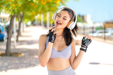 Young pretty sport woman at outdoors listening music with a mobile and singing