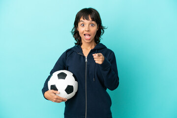 Young mixed race football player woman isolated on blue background surprised and pointing front