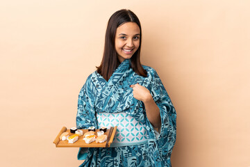 Woman wearing kimono and holding sushi over isolated background with surprise facial expression