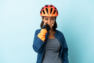 Young cyclist woman isolated on blue background happy and smiling covering mouth with hand