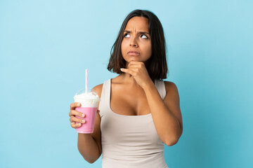 Young woman with strawberry milkshake isolated on blue background having doubts and with confuse...