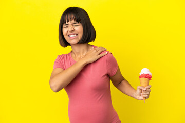 Pregnant woman holding a cornet ice cream isolated on yellow background suffering from pain in shoulder for having made an effort