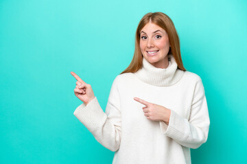 Young redhead woman isolated on blue background frightened and pointing to the side