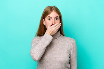 Young redhead woman isolated on blue background covering mouth with hand