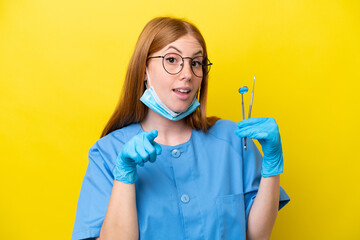 Young redhead Dentist woman isolated on yellow background surprised and pointing front