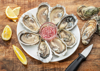 Opened raw oysters with sauce and lemon slices on plate on wooden table. Top view. © volff