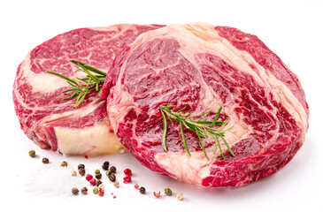 Raw beef steaks with herbs and spices ready for cooking on white background.