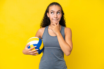 Young woman playing volleyball isolated on yellow background having doubts and thinking
