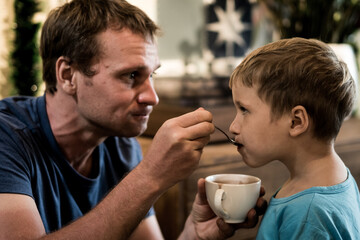 Father is feeding son by chocolate drink. Funny lifestyle moments. Happy childhood family education