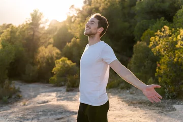 Selbstklebende Fototapeten Entspannung An attractive man breathes fresh air from nature at sunset. Healthy lifestyle and emotional well-being   © Laia Balart