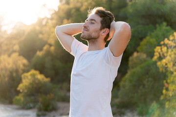 An attractive man breathes fresh air from nature at sunset. Healthy lifestyle and emotional well-being
