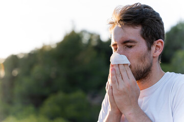 Sick man surrounded by nature blowing his nose and sneezing for pollen allergy symptoms