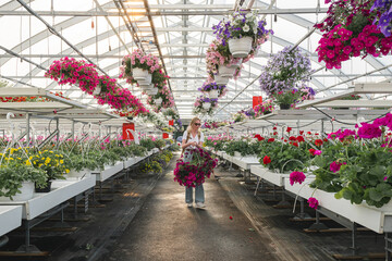 Young woman choosing beautiful colorful flower in garden greenhouse