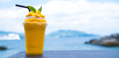 Smoothie made from fresh mango fruits against the backdrop of a seascape. Fruit and yoghurt ice...