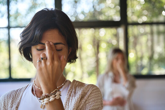 Young woman meditating with eyes closed doing yoga pranayama breathing exercises holding fingers on face feeling energy during holistic healing yoga training class retreat session. Close up view.