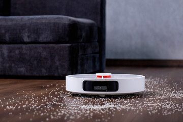 Robot vacuum cleaner vacuums the floor near the sofa. A smart home with automated devices that make...