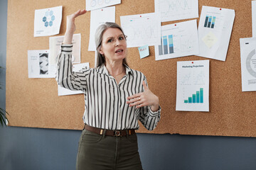 Mature woman, presentation and graphs on board for progress, sales or results in office. Female...