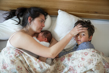 Mother laying in bed with newborn baby and older son, sharing an intimate and nurturing moment. The...