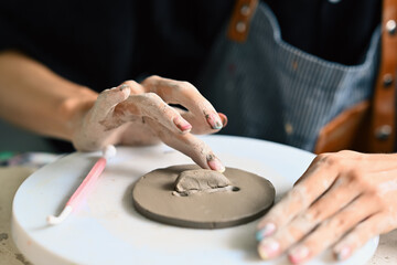 Close-up image, an individual's hands are delicately shaping a piece of clay on a rotating pottery...