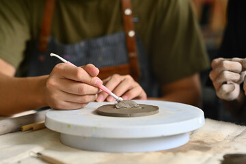 Close-up of an artist's hands sculpting clay on a pottery wheel, using a sculpting tool, showcasing...