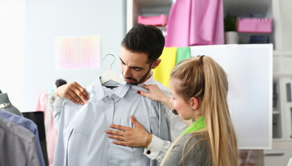 Obraz premium Assistant Buyer Fashion Dressmaker Sewer Service. Caucasian Stylist Standing near Male Purchaser Fitting on Formal Shirt. Girl Designer Consulting about Outfit. Couple at Dressmaking Atelier