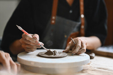A Close-up of a student artist's hands focuses on sculpting clay with precision, using a tool to shape pottery piece. Learning process in an art studio, creativity, skill development, and dedication