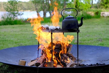 An old metal kettle stands among the flames of the fire. There's grilled food in aluminum foil....