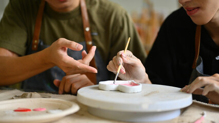 A close-up of Two students painting ceramic heart-shaped pieces with a brush together in an art...