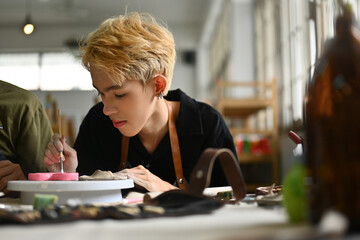 A focused art student meticulously paints a ceramic piece during art class hours, showcasing...