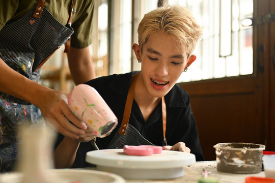 Young Artist Enjoying Pottery Making with a Helping Hand in a Creative Workshop