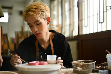 Focused LGBT teenage student working on a clay piece during art class, representing dedication and...