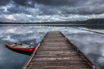 Naklejka premium a wooden dock next to a lake under cloudy skies with a red boat