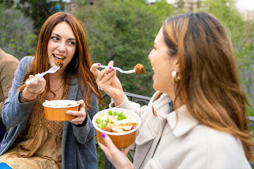 Two women enjoying lunch with eco-friendly utensils - using recyclable paper bowls and compostable...